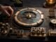A hand calibrates a wordless brass-and-graphite automation system on a dark workbench.