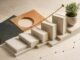 Five blank hardcover books arranged as ascending steps beside a brass growth line and a small green plant.